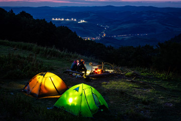 Summer evening in a hike. Glowing tents. Camping in a beautiful location. Sitting around the campfire.	