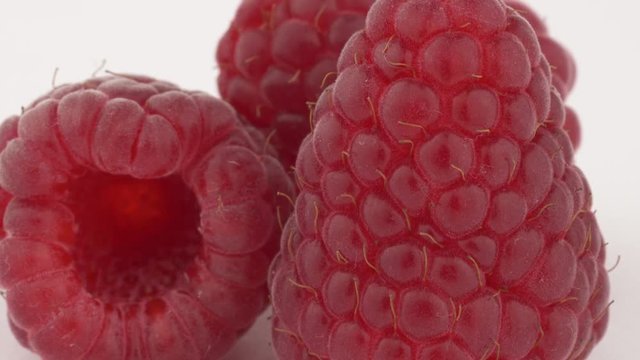 Fruits. A close-up of three tasty raspberries on rotating table. Isolated, on white background. Fresh summer berries