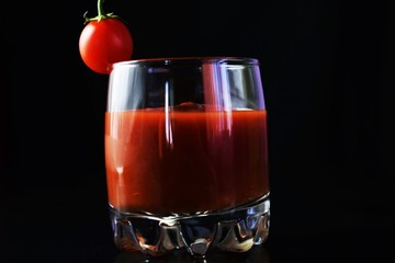 Fresh tomato juice in a glass glass on a black background and a small cherry tomato.