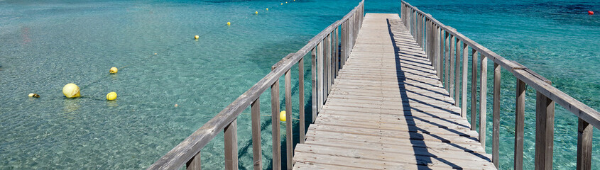 Obraz premium Panoramic image diminishing perspective wooden boardwalk empty path through turquoise Mediterranean Sea, cropped wide view. Palma de Mallorca, Majorca Balearic Islands, Spain 