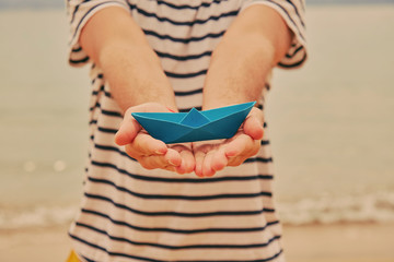 Man holding paper boat on tropical beach.