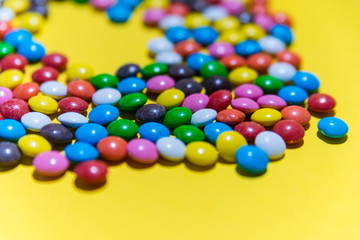 Obraz premium Colorful background of multicolored candy dragees. Round scattered sweets on a yellow bright background. Happy multicolor texture. Sweet candy wallpaper. Shallow depth of field. Flat lay on surface