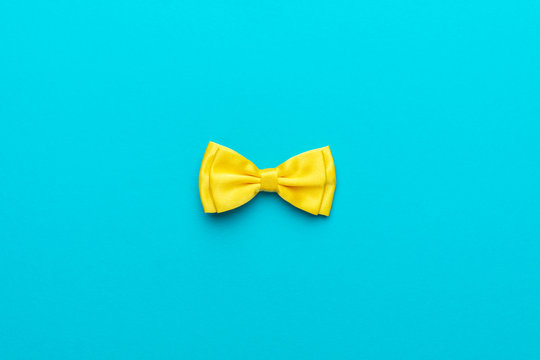 Minimalist flat lay photo of yellow satin bow tie over turquoise blue background and copy space. Top view and central composition of fashionable yellow men's accessory.