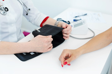 Professional female doctor putting on device for measuring pressure on young female patient hand in hospital room