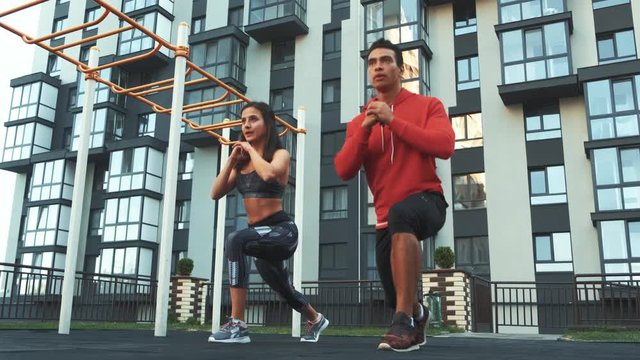 Image of young sporty man and woman 20s in tracksuits doing workout and squatting together