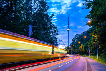 Germany, Illuminated tramway passing by street of traffic next to television tower of stuttgart...