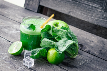 Green apple smoothie in glass and kale leaves on wooden table