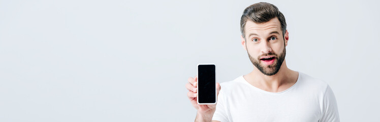 Obraz premium panoramic shot of shocked man showing smartphone with blank screen isolated on grey