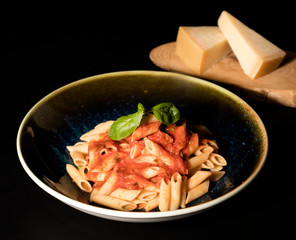 Homemade pasta with tomato sauce in a black plate on a black table served with kashar cheese on a wooden cutting board_2