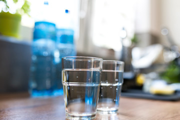 Two glasses of water in kitchen, with tap water and two bottles of mineral water. Shallow depth of field. Water shortage concept, saving water. Body hydration with clean & clear water.