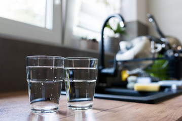 Two glasses of water in kitchen, with tap water and two bottles of mineral water. Shallow depth of field. Water shortage concept, saving water. Body hydration with clean & clear water.