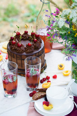 Summer picnic on nature, with a delicious chocolate cake, compote, berries, wild flowers