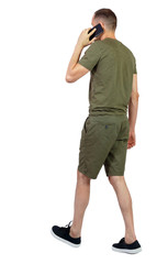 Back view of man in shorts walking with a mobile phone.