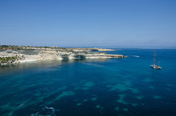 Fototapeta na wymiar Boat with landscape with Mediterranean Sea with blue water and white rocks in Malta near Marsaxlokk, Saint Peter Pool.