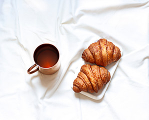 Morning breakfast flat lay with a cup of tea and croissants. Top view on the bed sheets