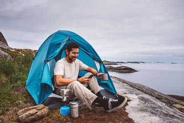 Smiling man using smartphone while sitting in camping tent