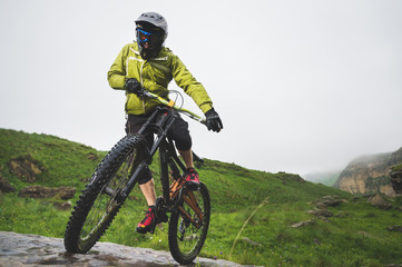 Fototapeta na wymiar Front view of a man on a mountain bike standing on a rocky terrain and looking down against a gray sky. The concept of a mountain bike and mtb downhill