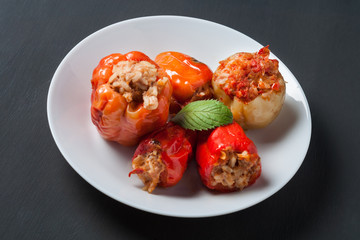 Portion of stuffed pepper, mint lies on round white ceramic plate and dark concrete table