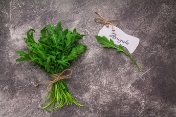 Bouquet of arugula tied with string of twine on a gray concrete background with the name Rucola on white paper. Top view with copy space for your text