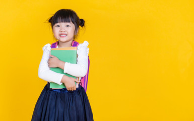 Portrait of young little asian girl hand holding books bag backpack isolated on yellow background...