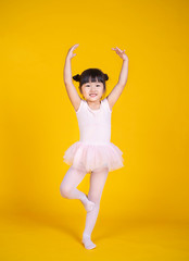Portrait of little asian child girl dreams of becoming ballerina in a pink tutu skirt isolated on yellow background. Happy young girl practise her dance. Education childhood toddler lifestyle concept © paulaphoto