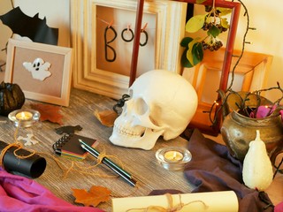 Decorative composition of the skull, pumpkins, lit candles, illumination, leaves and mystical decor on a gray wooden table and a light background, Halloween, autumn, October