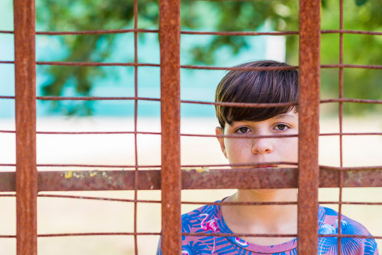 serious teen in casual wear behind metallic fence outdoors