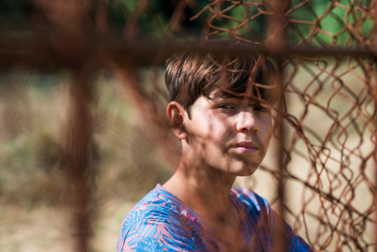 serious teen in casual wear behind metallic fence outdoors