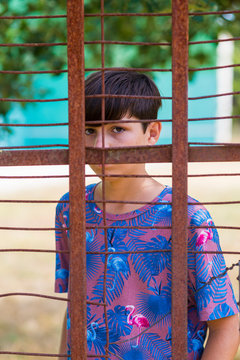 serious teen in casual wear behind metallic fence outdoors