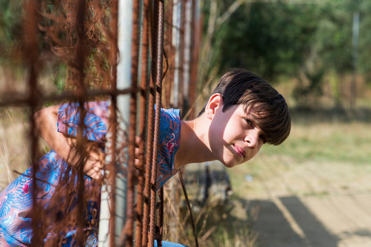 serious teen in casual wear behind metallic fence outdoors