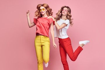 Obraz na płótnie Canvas Two easy-going happy hipster Woman dance Fun in Stylish fashion colored red yellow pants. Beautiful excited Girl in summer Trendy outfit, sneakers jump laughing. Creative dancing fashionable concept