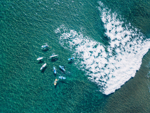 Aerial view of a group of surfers paddling on turquoise water surface