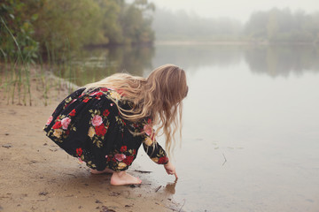 Blond girl dipping finger in lake