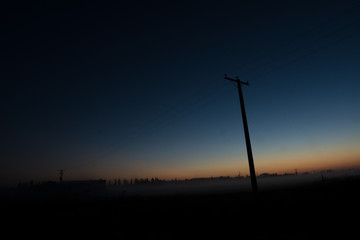 Un paisaje de anochecer en el que se ve una casa y un poste de electricidad