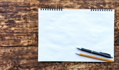 Empty notebook with a pencil and black pen on an old textural wooden surface.