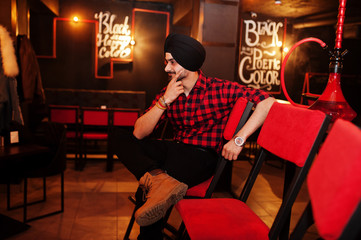 Indian man in checkered shirt and black turban sitting at bar.