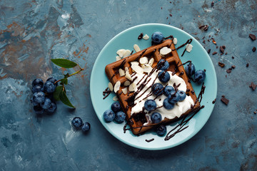 Chocolate belgian waffles with ice cream and fresh blueberry on blue background, top view