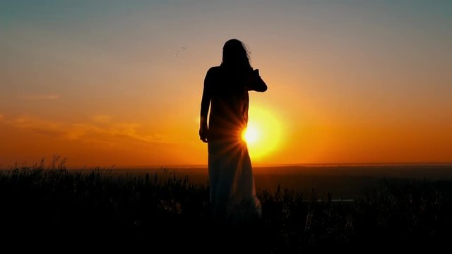 silhouette girl standing on the hill looking on amazing sky with rising sun female skirt and hair fluttering on the wind