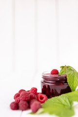preparations for the winter, raspberry berries lie near a jar of jam on a white table