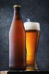 Bottle of light beer and a full glass of cold drink on a wooden table, close-up