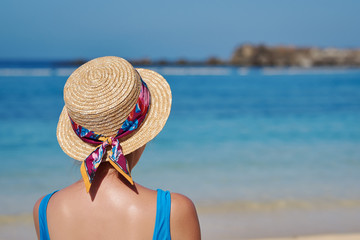 Young woman in sunhat relaxing on beach during summer vacation. She is against blue sea water on sunny day.