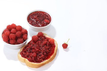 Red raspberries in a cup and toast with jam and fresh raspberries on a white isolated background, selective focus, copy space .