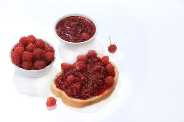 Red raspberries in a cup and toast with jam and fresh raspberries on a white isolated background, selective focus, copy space .