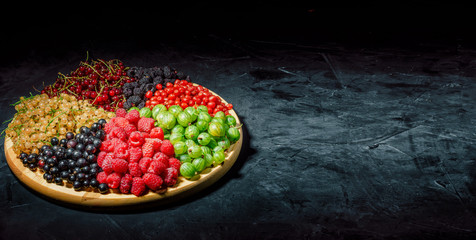 Berry assorted - mix of white and red currants, raspberries, strawberries, gooseberries on dark background