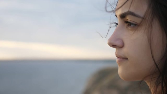 Inspired girl with fluttering hair looking at a huge sea at sunset in slo-mo  