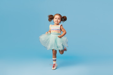 Little happy toddler child girl dreams of becoming ballerina in a cyan tutu skirt. Blue background....