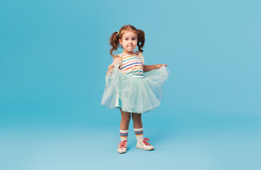 Little happy toddler child girl dreams of becoming ballerina in a cyan tutu skirt. Blue background. Space for text - obrazy, fototapety, plakaty