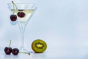 Dry martini with two red cherry berries. Kiwi next to a martini glass. Cocktail party. 
