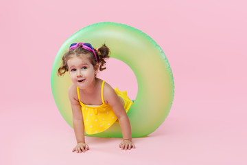 Obraz na płótnie Canvas Happy pleased toddler girl in yellow swimsuit with inflatable circle donut on a colored pink background. Summertime vacation and travel concept