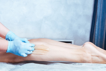 Beautician depilating young woman's legs with liquid sugar in spa center